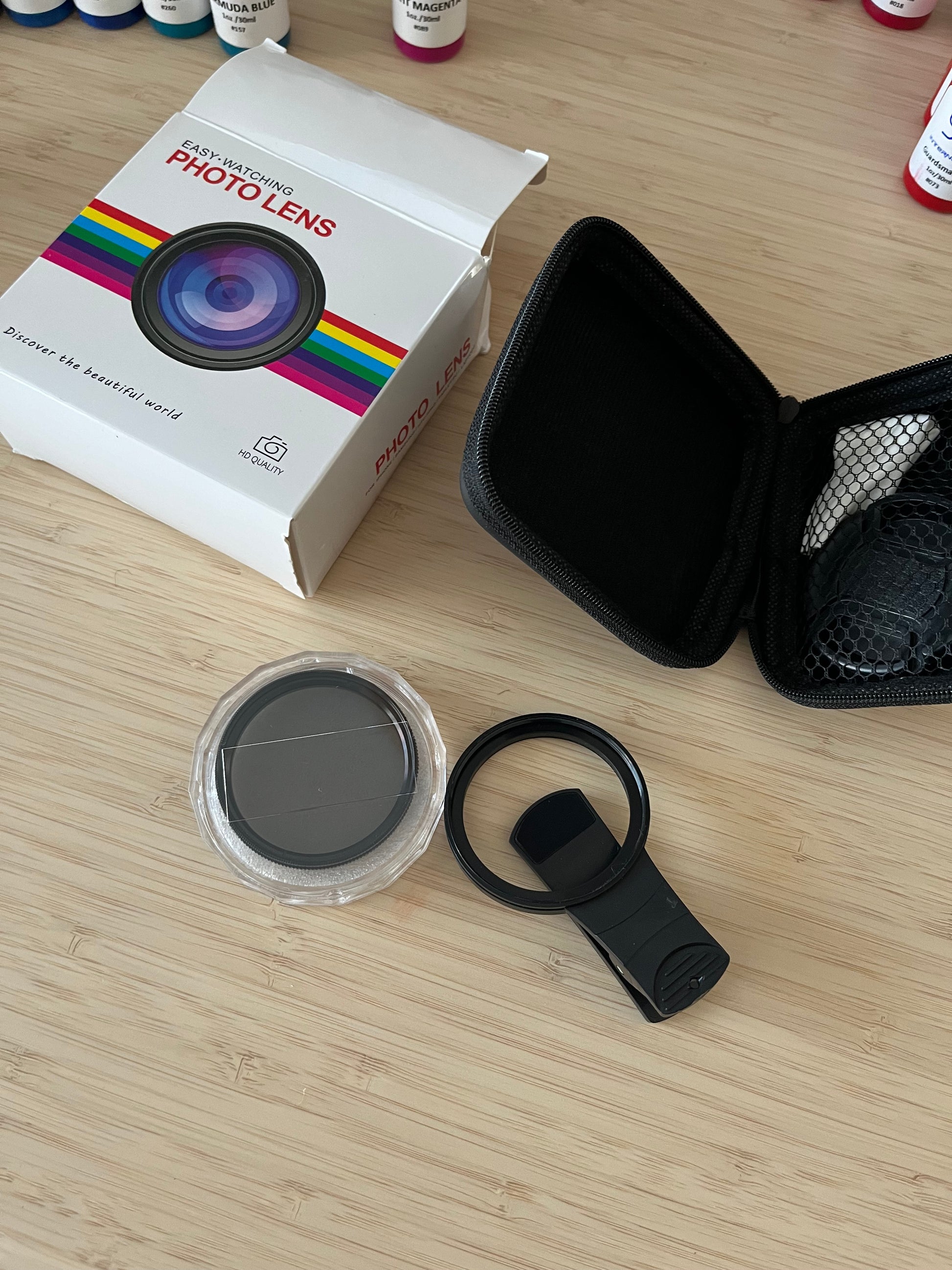 Image of a mobile phone photo lens kit showing the full contents, including a clip-on lens, lens cover, and an open protective case. The white packaging box labeled "Easy-Watching Photo Lens" is displayed in the background. Perfect for mobile photography enthusiasts.