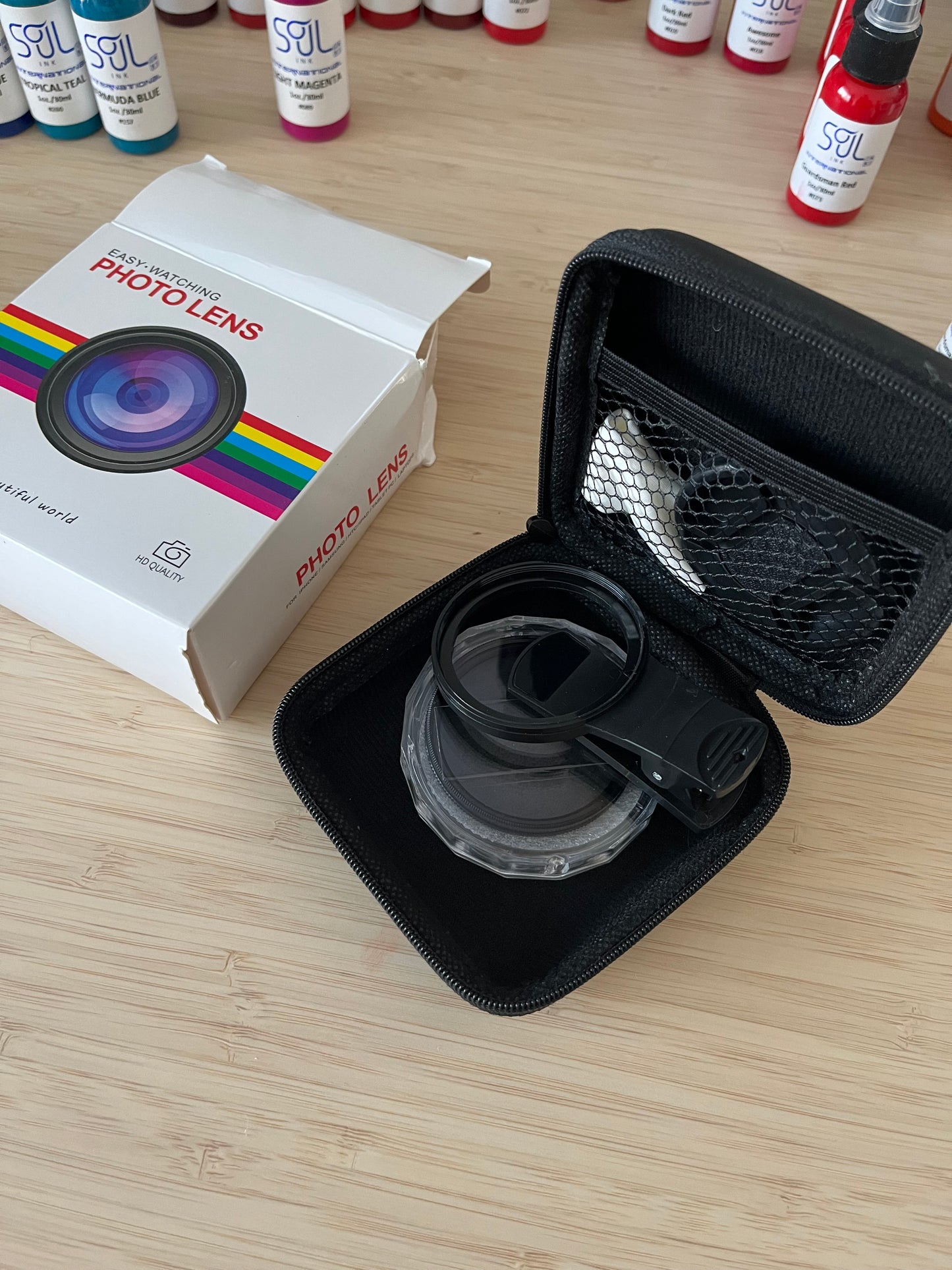 Image of a mobile phone photo lens kit, showing an open black protective case with a clip-on lens inside. The white packaging box labeled "Easy-Watching Photo Lens" is visible in the background. Ideal for enhancing mobile photography.