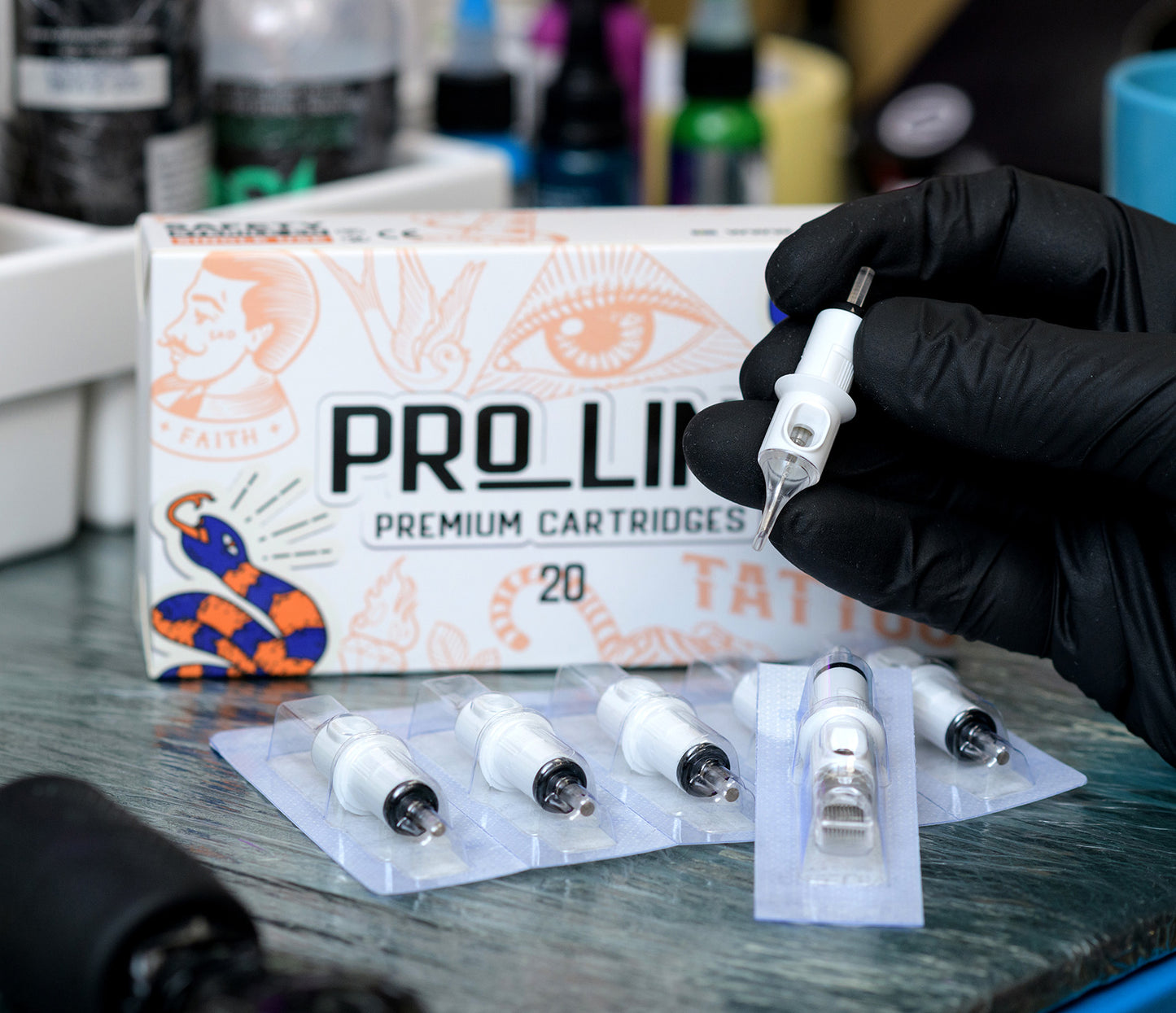 Photograph featuring a hand wearing black gloves holding a Pro-Line Premium Cartridges cartridge. Below the hand, various cartridges with packages are arranged, showcasing the product range. In the background, a Pro-Line Premium Cartridges box is visible, adding context to the assortment. The composition highlights the brand's diversity and quality.