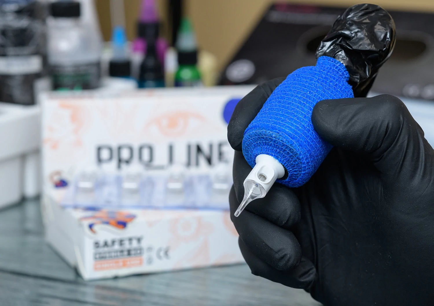 Close-up view of a Pro-Line Premium Cartridges cartridge, held by a hand wearing black gloves. The cartridge is the focal point of the image, displaying intricate details and branding. In the background, multiple Pro-Line Premium Cartridges boxes are stacked, adding context to the product's availability.