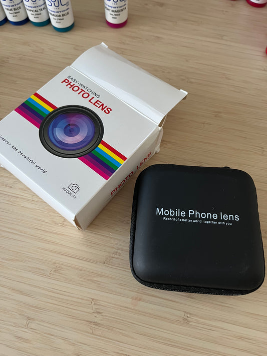 Image of a mobile phone photo lens kit, including a black protective case labeled "Mobile Phone Lens" and a white box with rainbow accents labeled "Easy-Watching Photo Lens." Ideal for enhancing mobile photography.